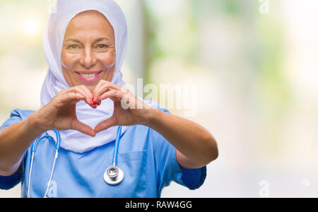 Mittleres Alter älteren arabischen Krankenschwester Frau, tragen, Hijab über isolierte Hintergrund lächelnd in Liebe mit Herz und Formen mit den Händen. Romantische Konzept. Stockfoto