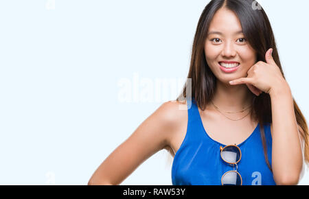 Junge asiatische Frau über isolierte Hintergrund lächelnd tun Telefon Geste mit der Hand und der Finger wie im Gespräch am Telefon. Verbreitung von Konzepten. Stockfoto