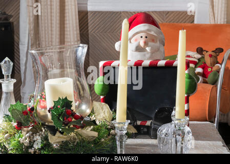 Weihnachtsmann auf einen Tisch, halten eine Tafel mit anderen Weihnachtsdekorationen Sitzen Stockfoto