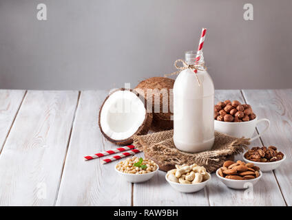 Vegan Milch von Muttern in der Flasche mit der Roten abgestreift Stroh um verschiedene Nüsse auf weissem Holztisch Stockfoto