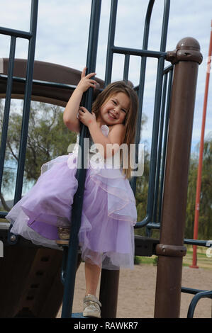 Junge Mädchen greifen ein Pole auf einem Spielplatz in einem Princess Dress Stockfoto