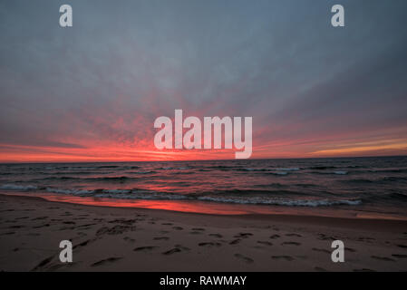 Sonnenuntergang am Lake Michigan reflektiert über den See und den Strand entlang mit tiefen Pinks das meiste Wasser bedecken. Stockfoto