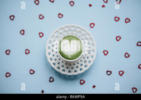 Frischer grüner Matcha Tee mit Herz Muster auf einer festlichen Hintergrund mit vielen Herzen. Konzept für den Valentinstag oder Tag der Frauen. Stockfoto