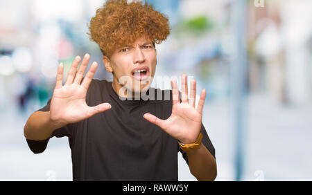 Junger stattlicher Mann mit afro Haar zu tragen schwarze t-shirt Angst und Furcht Ausdruck stop Geste mit den Händen, Angst, Schreien im Schlag. Panik co Stockfoto