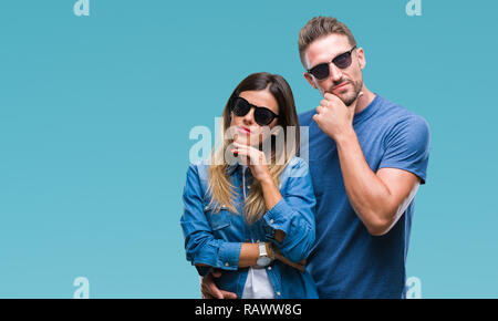 Junges Paar in der Liebe tragen Sonnenbrillen über isolierte Hintergrund mit der Hand am Kinn über die Frage denken, nachdenklichen Ausdruck. Lächelnd mit thoughtfu Stockfoto