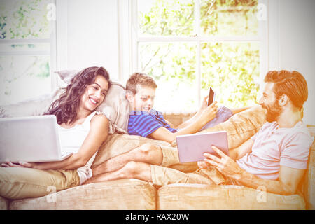 Freundliche Familie mit Technologien beim Liegen auf dem Sofa Stockfoto