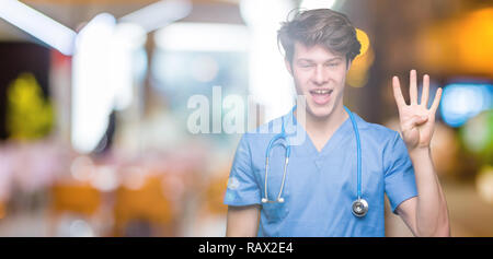 Junger Arzt mit medizinischen gleichmäßig über isolierte Hintergrund angezeigt und zeigen mit den Fingern Nummer vier, während lächelte zuversichtlich und fröhlich. Stockfoto