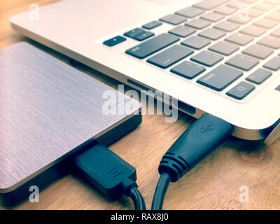 Externe oder tragbare Festplatte (HDD) auf Laptops für die Übertragung und Sicherung von Daten auf Holz- Textur office Desktop angeschlossen Stockfoto