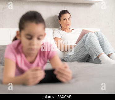 Porträt eines einzigen weißen Mutter das Lesen eines Buches an ihrer Tochter mit Ihrem Mobiltelefon und zu viel Zeit im Internet suchen. Übergeordnete Aufsicht aus Technik und Social Media gefahren. Adhs Stockfoto