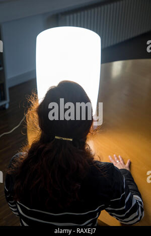 Die Lichttherapie mit Tageslicht Lampe, eine Frau sitzen vor eine Lampe, die Tageslicht imitiert, Therapie gegen Winter Depression, weil zu wenig Stockfoto