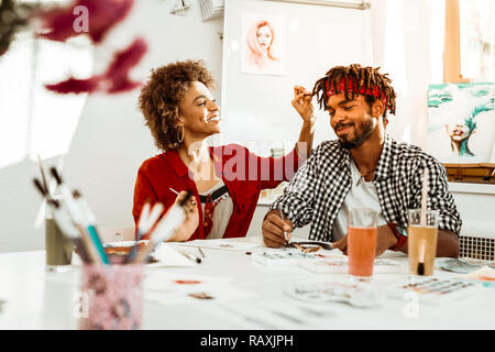 Lächelnde niedliche Freundin berühren Dreadlocks ihres Mannes Stockfoto