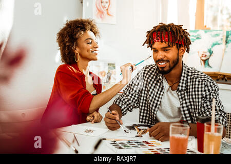Fröhliche strahlende Freundin Streiche spielen, während ihr Mann Färbung Stockfoto