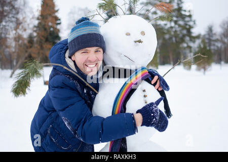 Junge europäische Mann in warme Kleidung, Schneemann aus Schnee outdoor. Spaß wie ein Kind im Winter Urlaub. Stockfoto