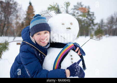 Junge europäische Mann in warme Kleidung, Schneemann aus Schnee outdoor. Spaß wie ein Kind im Winter Urlaub. Stockfoto