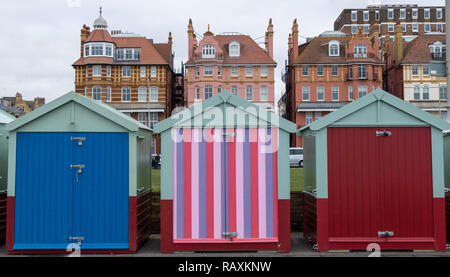 Wooden Badekabinen, einige in Candy stripes bemalt, am Meer in Hove, East Sussex, UK. Der Wohnblock hinter sich. Stockfoto