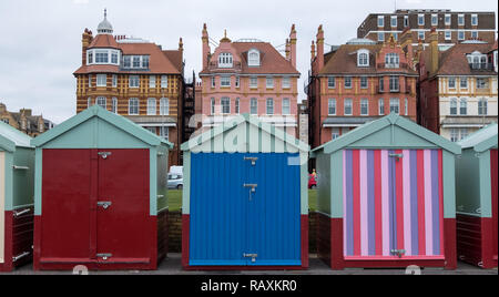 Wooden Badekabinen, einige in Candy stripes bemalt, am Meer in Hove, East Sussex, UK. Der Wohnblock hinter sich. Stockfoto