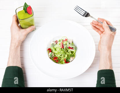 Mann mit grünen Smoothie und beim Verzehr von rohen vegan Spaghetti von Zucchini, sonnengetrocknete Tomaten und Mutter Käse auf weißem Hintergrund im Restaurant Stockfoto