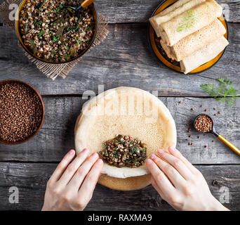 Frau rolling Russischen vegane Pfannkuchen mit Buchweizen und Laminaria im rustikalen Stil auf Fastnacht Feiertage serviert. Stockfoto