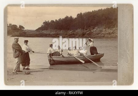 Frühe edwardianische Kabinettkarte von 7 jungen Damen und Mädchen mit langen Röcken und Strohboatern, die sich amüsieren und ein Ruderboot in Mill Bay, Salcombe, Devon, Großbritannien, im Sommer Juni 1901 landen Stockfoto