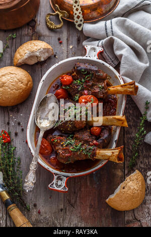 Lammkeule in reichen Tomatensauce mit Brot und Kräutern, Ansicht von oben. Stockfoto