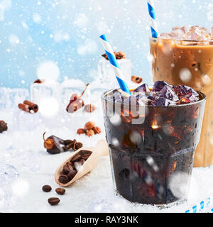 Winter trinke Eiskaffee in einem Glas Kaffee mit Sahne und Eis in ein hohes Glas mit Eis, Kaffee Bohnen und verschiedenen Gewürzen auf weißem Marmortisch umgeben Stockfoto