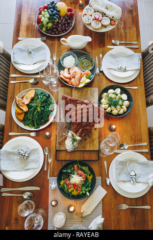 Moderne australische Weihnachtsessen Tabelle mit glasierten Schinken, Garnelen, Kartoffeln und Dill, asiatische Grüns, Christmas Pudding, Hackfleisch Obstkuchen bei Kerzenschein. Stockfoto