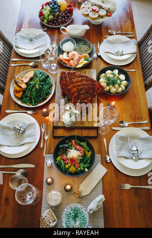 Moderne australische Weihnachtsessen Tabelle mit glasierten Schinken, Garnelen, Kartoffeln und Dill, asiatische Grüns, Christmas Pudding, Hackfleisch Obstkuchen bei Kerzenschein. Stockfoto