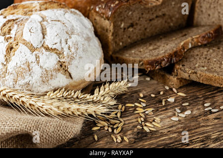 Gruppe von dunklen Brote mit Weizen, Sonnenblumen und Roggen Getreide auf einer hölzernen vintage Tabelle. Stockfoto