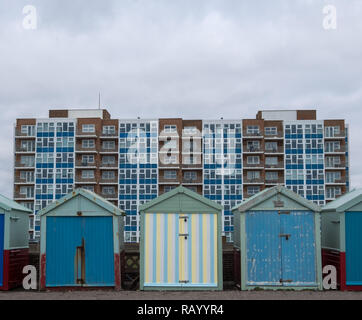 Wooden Badekabinen, einige in Candy stripes bemalt, am Meer in Hove, East Sussex, UK. Der Wohnblock hinter sich. Stockfoto