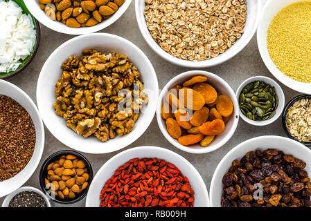 Vegetarisches Frühstück mit gesunden Lebensmitteln Auswahl, Nüsse, Samen, Getreide, Früchte, Aprikosen, Goji Beeren, Nüssen und anderen Superfoods auf Tisch, flach Stockfoto