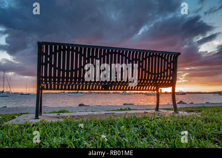 Isolierte Parkbank im öffentlichen Park bei Sonnenuntergang in Sarasota, Florida mit dramatischen Himmel Stockfoto