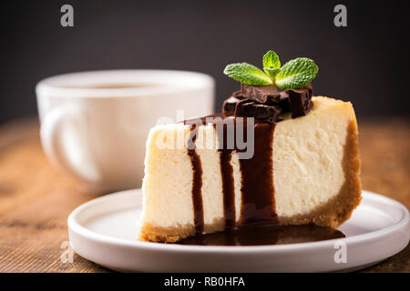 Käsekuchen mit Schokoladensauce und Tasse Kaffee. Scheibe des klassischen New York Cheesecake mit Schokoladensauce gegossen und mit minzeblatt eingerichtet Stockfoto