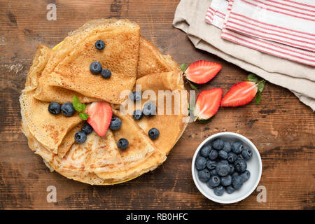 Crepes, dünne Pfannkuchen oder russische blini mit frischen Beeren auf alten Holztisch Hintergrund. Ansicht von oben Stockfoto