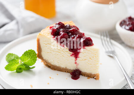 Lecker New York Cheesecake mit Kirschsoße auf weiße Platte. Detailansicht. Klassische Käsekuchen mit süßen Beeren-Sauce Stockfoto
