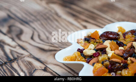 Getrocknete Früchte in Weiß Platte auf dem Holztisch. Mischung von verschiedenen Sorten von Nüssen und Beeren, Vitamine. Mit Platz für Text kopieren Stockfoto