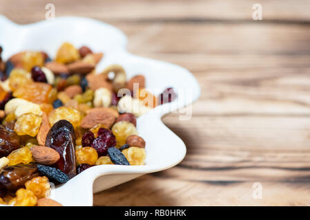 Mischung von Nüssen und Beeren. Getrocknete Früchte in Weiß Platte auf dem Holztisch. Gesunde Ernährung und Vitamine. Kopieren Sie Platz für Text Stockfoto