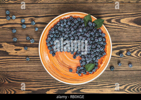 Vielen saftigen schönen erstaunlich schöne Blaubeeren in orange Platte auf dunklem Hintergrund. Schönes essen Kunst Hintergrund. Ansicht von oben, kopieren. Stockfoto