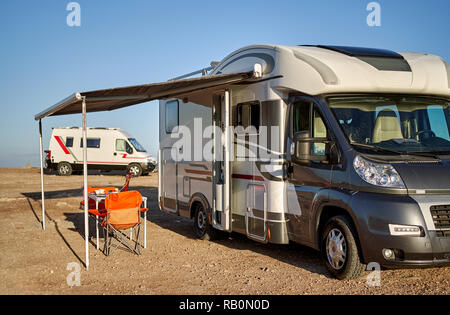 Leere faltbare Stühle und Tisch unter dem Vordach in der Nähe von neuen modernen recreational vehicle Camper Trailer. Abenteuer, aktive Menschen reisen mit Motor home Conc Stockfoto