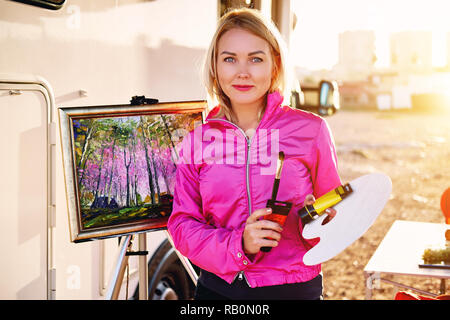 Ziemlich Maler im mittleren Alter blonde Frau hält Pinsel, Palette, in der Nähe von Bild auf Leinwand bei Camera suchen Stockfoto