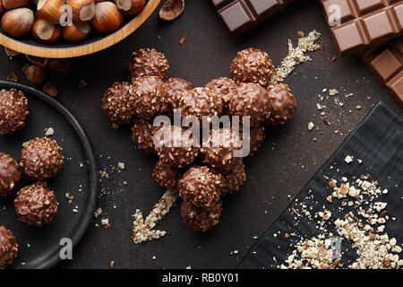 Herz mit Pfeil von Schokolade Trüffel Bonbons mit Haselnüssen und Mutter crumb auf Braun strukturierten Hintergrund gemacht, Ansicht von oben Stockfoto