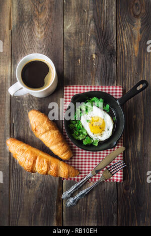 Das traditionelle Frühstück mit Kaffee, Croissants und Spiegelei in Iron Skillet auf rustikalen Holzmöbeln Hintergrund. Stockfoto