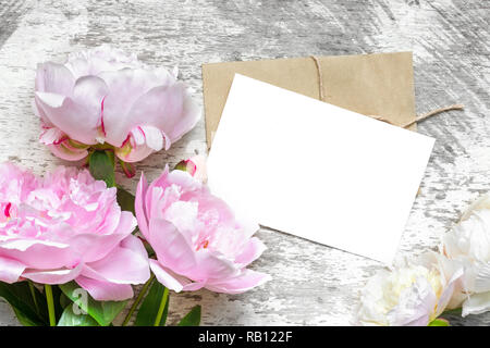 Leere weiße Grußkarte mit rosa Pfingstrose blumen blumenstrauss und Umschlag auf weißem Holz- Hintergrund. Flach. top anzeigen. Mock up Stockfoto