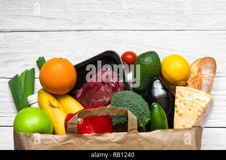 Full Paper bag verschiedener gesundes Essen auf weißem Holz- Hintergrund. Obst, Gemüse und Rindfleisch. Ansicht von oben. Flach Stockfoto