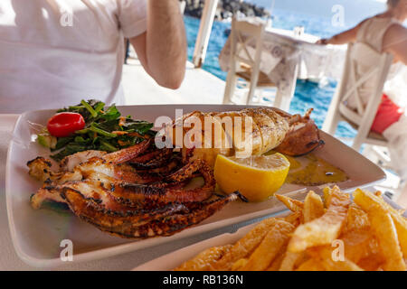Essen gegrillten Calamari squid in einem Seafood Restaurant durch die Kosten in Santorin Oia Amoudi Bucht Meer Hintergrund Stockfoto