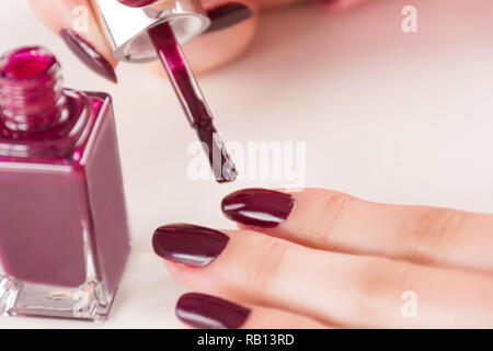 Weibliche mit Pinsel und Flasche Rotwein anwenden Maniküre Nägel polieren am Finger auf weißem Schreibtisch. Maniküre und Mädchen Mode und Schönheit Konzept Stockfoto