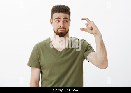 Innen- schuss unbeeindruckt cute bärtigen Kerl wartete etwas mehr Form kleine oder winzige Objekt an der Hand mit Grinsen und unzufriedene Suchen als Mehr über weißen Hintergrund erwartet Stockfoto