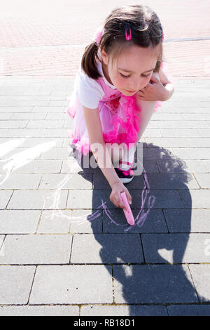 Schöne Mädchen zeichnen ein rosa Herz mit Kreide auf dem Bürgersteig. Stockfoto