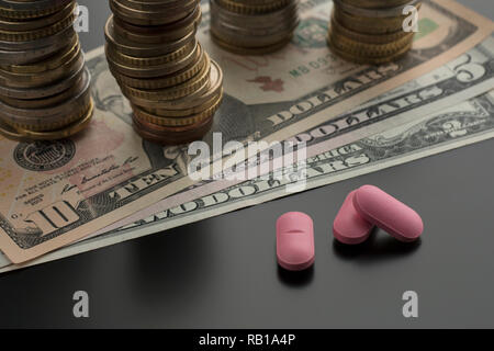 Rosa Pillen, Tabletten, Drogen mit Dollarnoten und Stapel von Münzen auf dem Hintergrund. Konzept der medizinischen Kosten Stockfoto