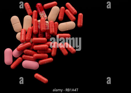 Ein Haufen von rot, beige, rosa Tabletten, Pillen oder Kapseln auf dem schwarzen Hintergrund. Für medizinische, pharmazeutische Themen, Gesundheit Stockfoto