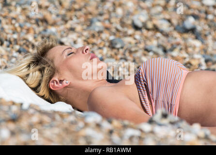 Junge hübsche Frau, die Festlegung auf den Rücken beim Sonnenbaden am Strand an einem warmen Tag im Frühjahr in Großbritannien. Stockfoto